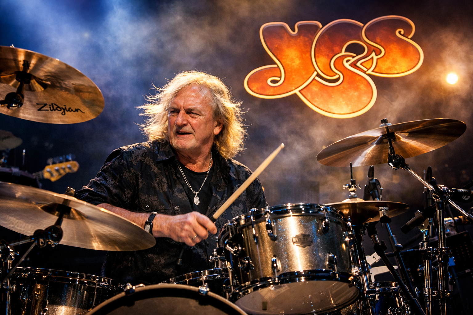 照明に包まれステージでドラムを演奏する長髪の男性